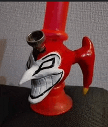 a red bong with a clown face on it is sitting on top of a couch .