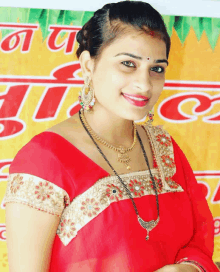 a woman wearing a red top and gold jewelry smiles in front of a sign that says ' a '