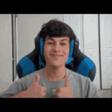 a young man wearing headphones is giving a thumbs up sign while sitting in a blue chair .