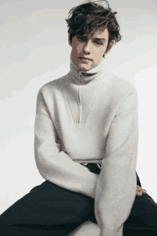 a young man wearing a white sweater and black pants is sitting down