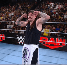 a man in a black tank top and white shorts stands in a wrestling ring in front of a sign that says raw