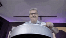 a man wearing glasses is playing a drum in front of a purple light