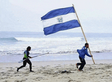 a man carrying a large blue and white flag on the beach