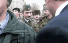 a man in a suit stands in a crowd of soldiers with the name sladkov + written on the back of his jacket