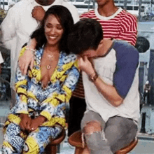 a man is kissing a woman on the cheek while sitting on a stool in front of a group of people .