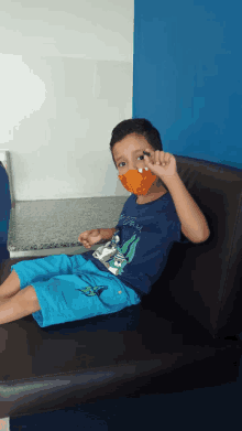 a young boy wearing a mask is sitting on a couch holding a green pencil