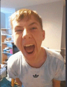 a young boy wearing an adidas shirt is making a funny face with his mouth open .