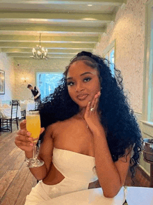 a woman in a white dress is sitting at a table holding a glass of champagne .