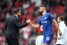 two soccer players are shaking hands on the field during a soccer match .