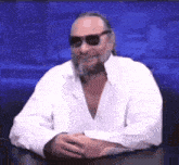 a man with a beard wearing sunglasses is sitting at a table .