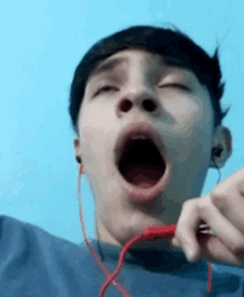 a young man wearing ear buds is yawning with his mouth open