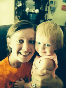 a woman holding a baby wearing an orange shirt that says age on it