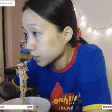 a woman wearing a shirt that says alien is eating noodles from a bowl