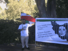 a man holds a flag in front of a sign that says " islamic republic of iran is a big prison for women "