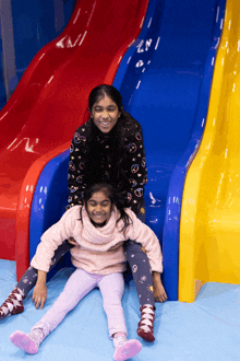 two little girls are playing on a slide and one of them is laying on the other 's lap