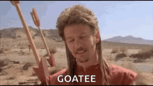 a man in a mullet is holding an arrow in the desert and says `` goatee '' .