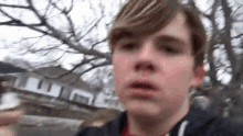 a young boy is standing in front of a house holding a hockey stick and looking at the camera .