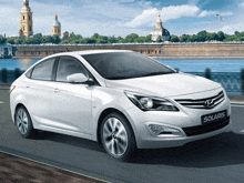 a white hyundai solaris is driving down a road near a body of water