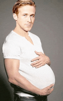 a pregnant man in a white shirt is holding his belly and looking at the camera .