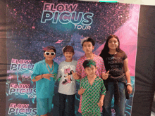 a group of young people pose in front of a flow picus tour sign