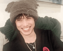 a young man wearing a hat and a necklace smiles