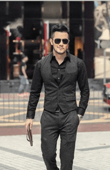 a man wearing a suit vest and sunglasses is walking down the street holding a wallet .