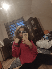 a girl wearing sunglasses takes a picture of herself in the mirror