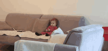 a baby is sitting on a grey couch