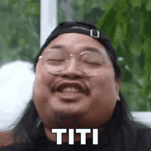 a man with long hair and glasses is making a funny face with the word titi written on his face .