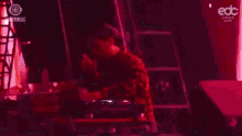 a man in a plaid shirt is playing a dj set on a stage in a dark room .