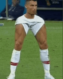 a man is standing on a soccer field with his legs crossed and his shorts ripped off .