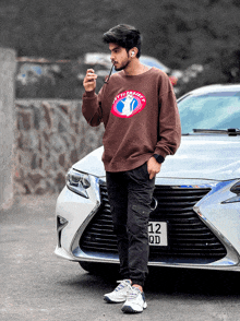 a man wearing a sweatshirt that says atti project stands in front of a white car