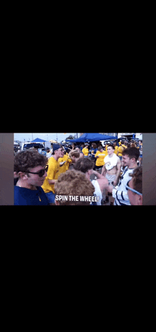 a group of people are standing in a crowd and one of them says spin the wheel .