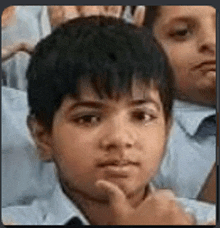 a young boy is sitting in a classroom with his hand on his chin and looking at the camera .