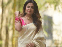 a woman wearing a white saree and a pink blouse is standing in a forest .