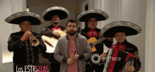 a man in a pink jacket stands in front of a group of mariachi players with the words " las estrellas " on the bottom