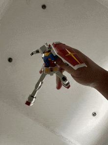 a person is holding a toy robot with a red and yellow cross on its shield