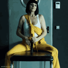 a woman in yellow pants and a white tank top is sitting on a chair with the words mxrirlento on the bottom