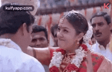 a bride and groom are standing next to each other at a wedding and the bride is wearing a garland .