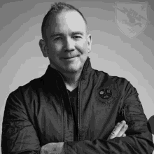 a black and white photo of a man wearing a bomber jacket with his arms crossed .