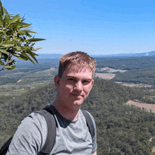 a man wearing a backpack stands on top of a hill overlooking a forest