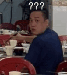 a man is sitting at a table in a restaurant eating food with chopsticks and a question mark above his head .