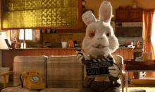 a rabbit is sitting on a couch holding a clapper board with the number 001 on it