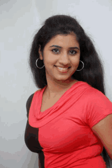 a woman in a red top and hoop earrings smiles for the camera