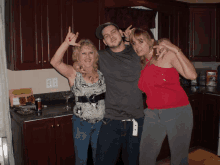 a man and two women pose for a photo in a kitchen with a can of coca cola in the background