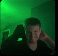 a man is smiling while sitting in a chair in a dark room with a green light behind him .