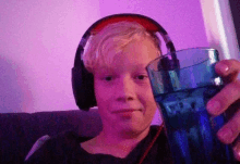 a young boy wearing headphones holds a blue glass of water