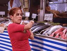 a woman in a red shirt stands in front of a fish counter with a sign that says salmao on it