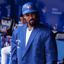 a man wearing a blue jays jacket and helmet stands in a dugout