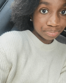 a woman wearing a white sweater and earrings looks at the camera